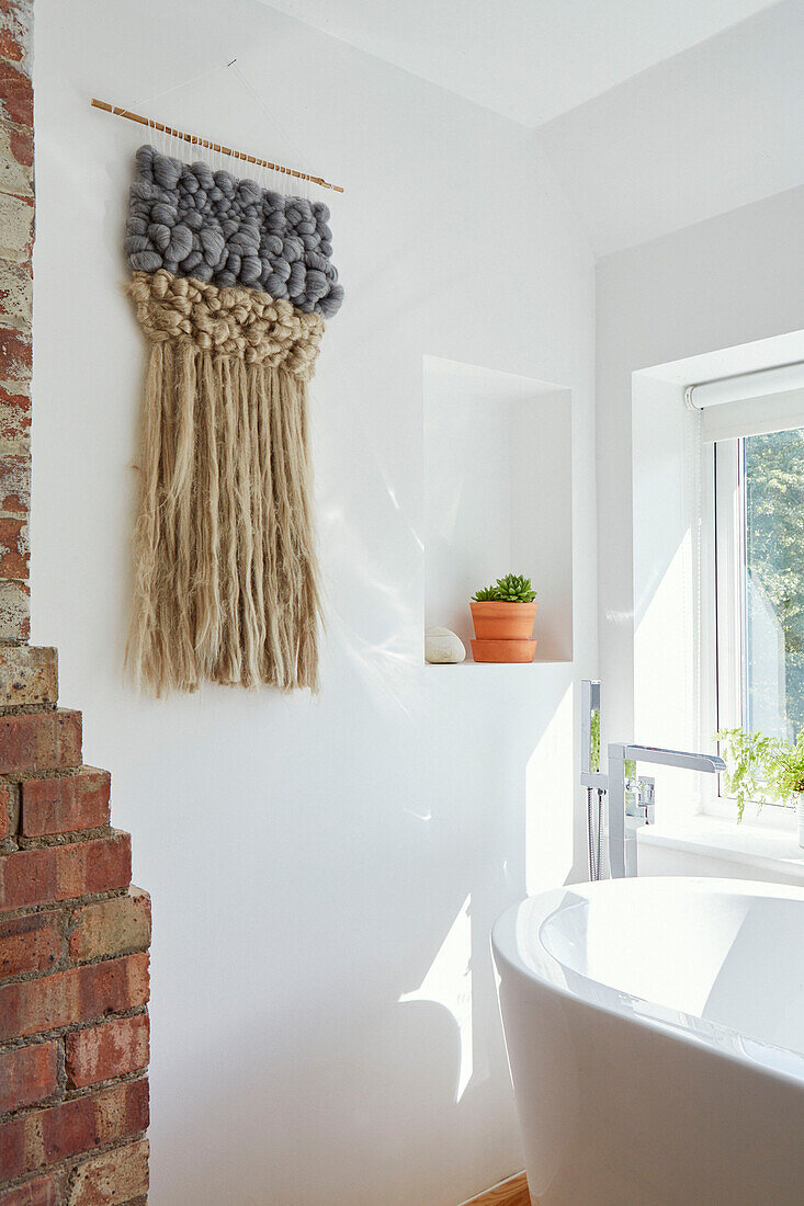 Woven wall hanging and exposed brick in white bathroom of Bath home, Wiltshire, UK