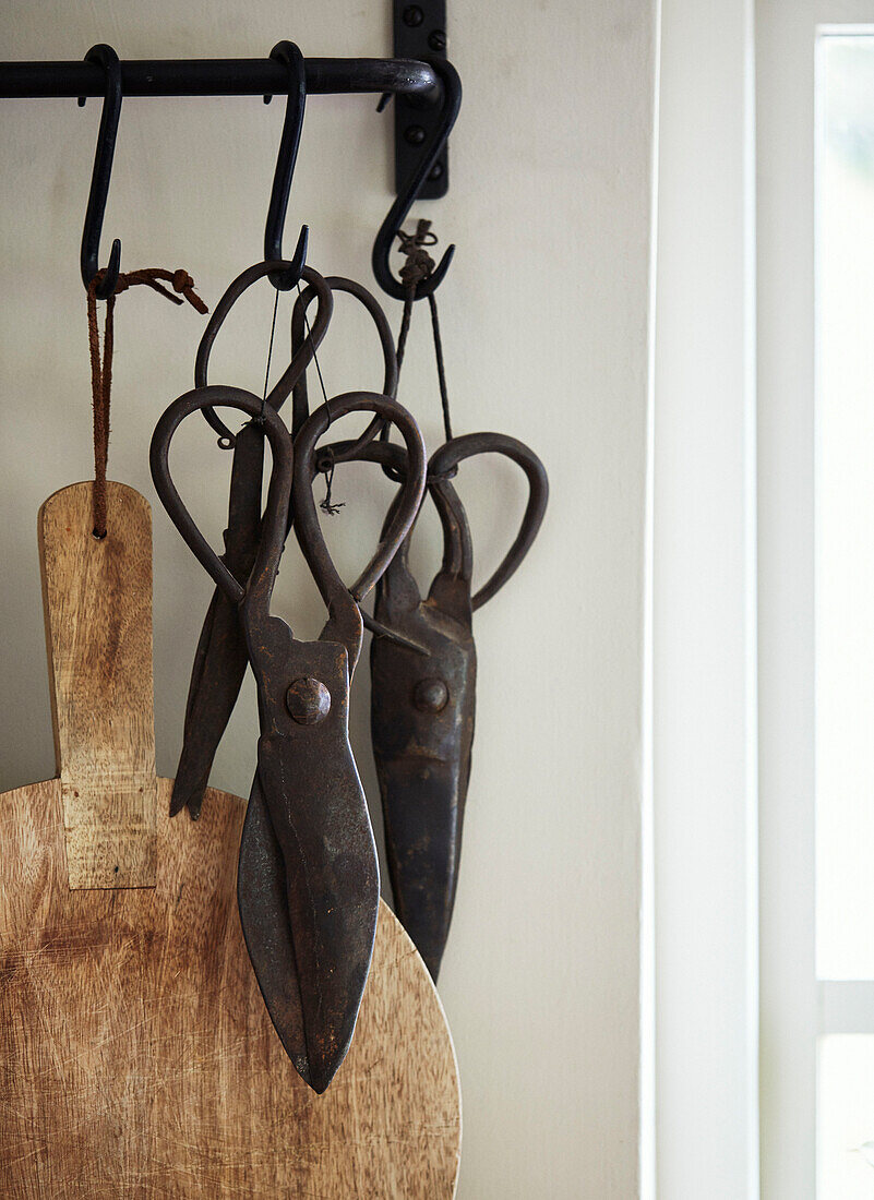 Vintage scissors and choppping board on black metal hooks in Devon kitchen, UK