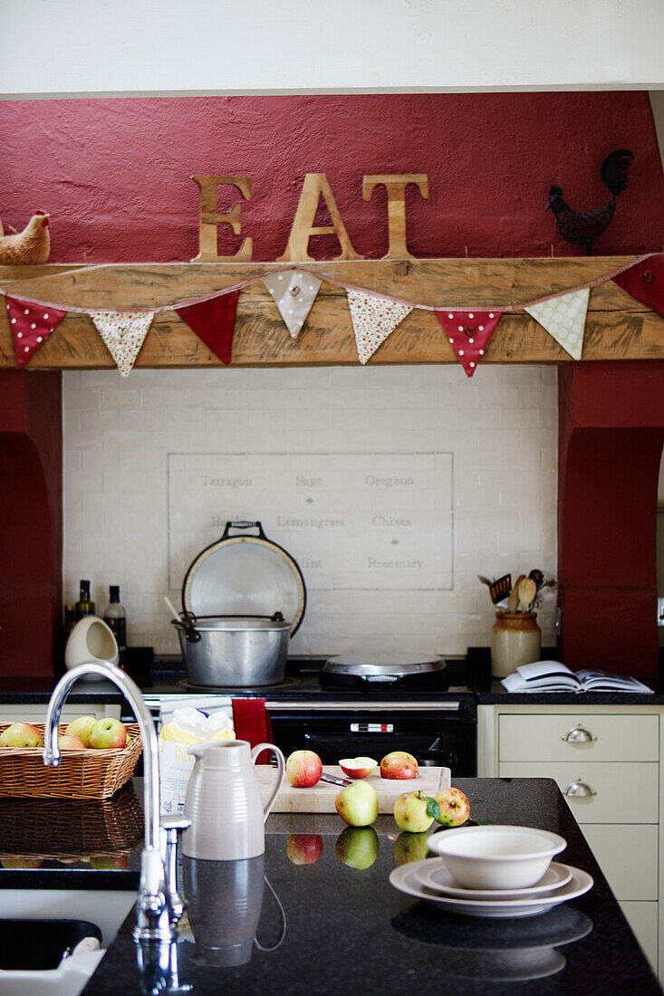 Geschnittene Äpfel auf einer Kücheninsel mit Wimpel über dem Ofen und dem Wort 'EAT' in einer Bauernhausküche in Northumberland, UK