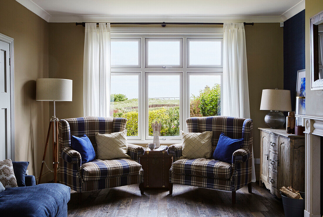 Blau und braun karierte Sessel mit Lampen im Fenster eines Hauses an der Küste von Northumbria, UK