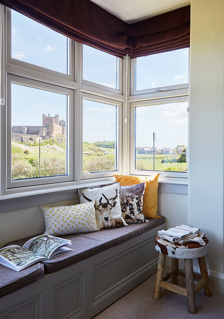 Bücher und Kissen auf einer Fensterbank mit Blick auf Bamburgh Castle in Northumbria, UK