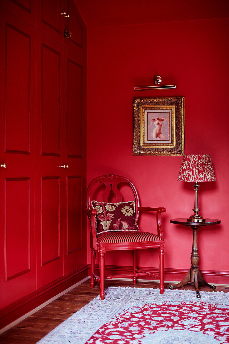 Lampe auf Beistelltisch mit rotem Stuhl und Schränken und vergoldetem gerahmten Bild in einem Cottage in den Cotswolds, UK