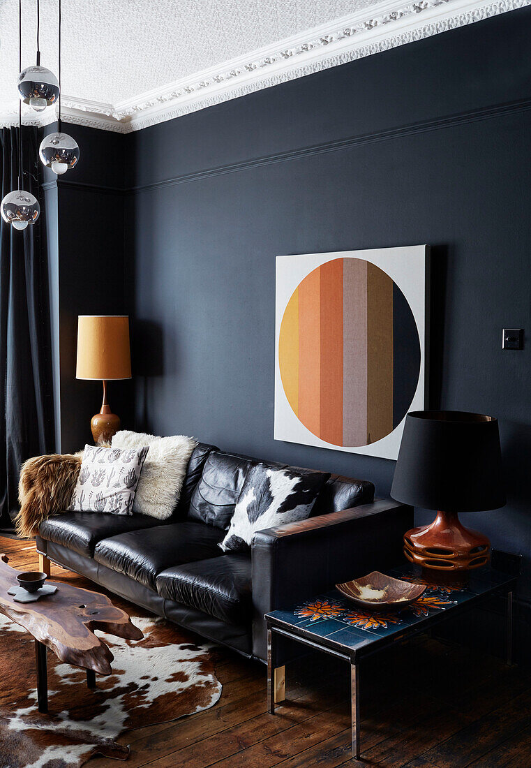 Moderne Leinwand über einem schwarzen Ledersofa mit Vintage-Lampen in einem Wohnzimmer in Ramsgate, Kent, UK