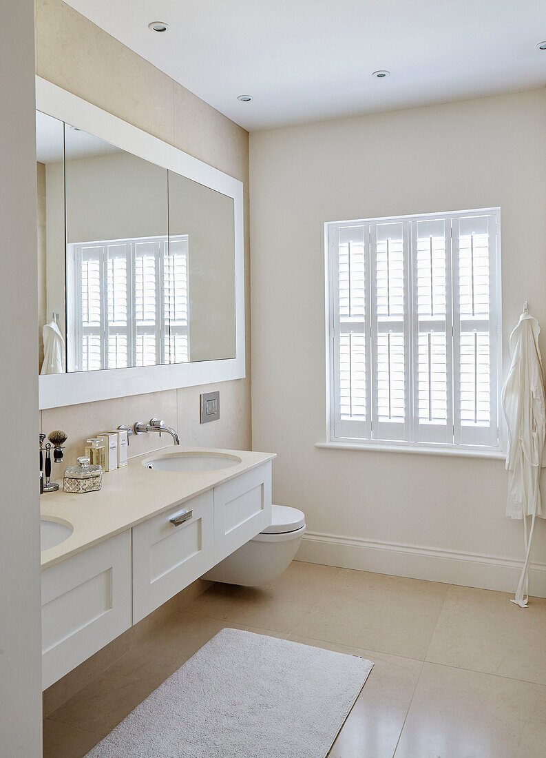 Mirrored cabinet above double basin with shutters in window of York home, UK