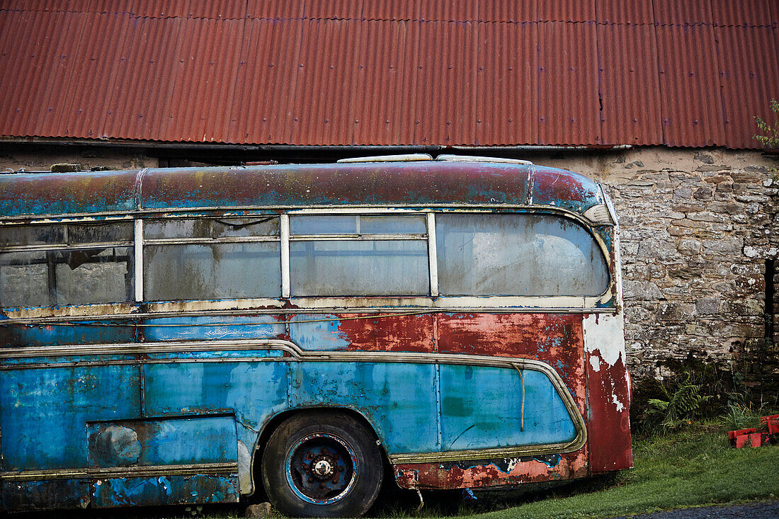 Alter blauer Bus vor einer Steinscheune mit Wellblechdach an der Grenze zwischen Radnorshire und Herfordshire