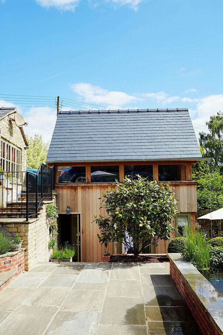 Gepflasterte Terrasse als Zugang zu einem holzverkleideten Neubau in den Cotswolds, UK