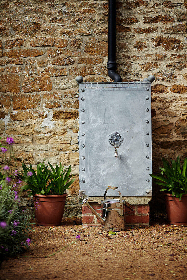 Metall-Wassertonne im Garten eines Steinhauses in den Cotswolds, UK