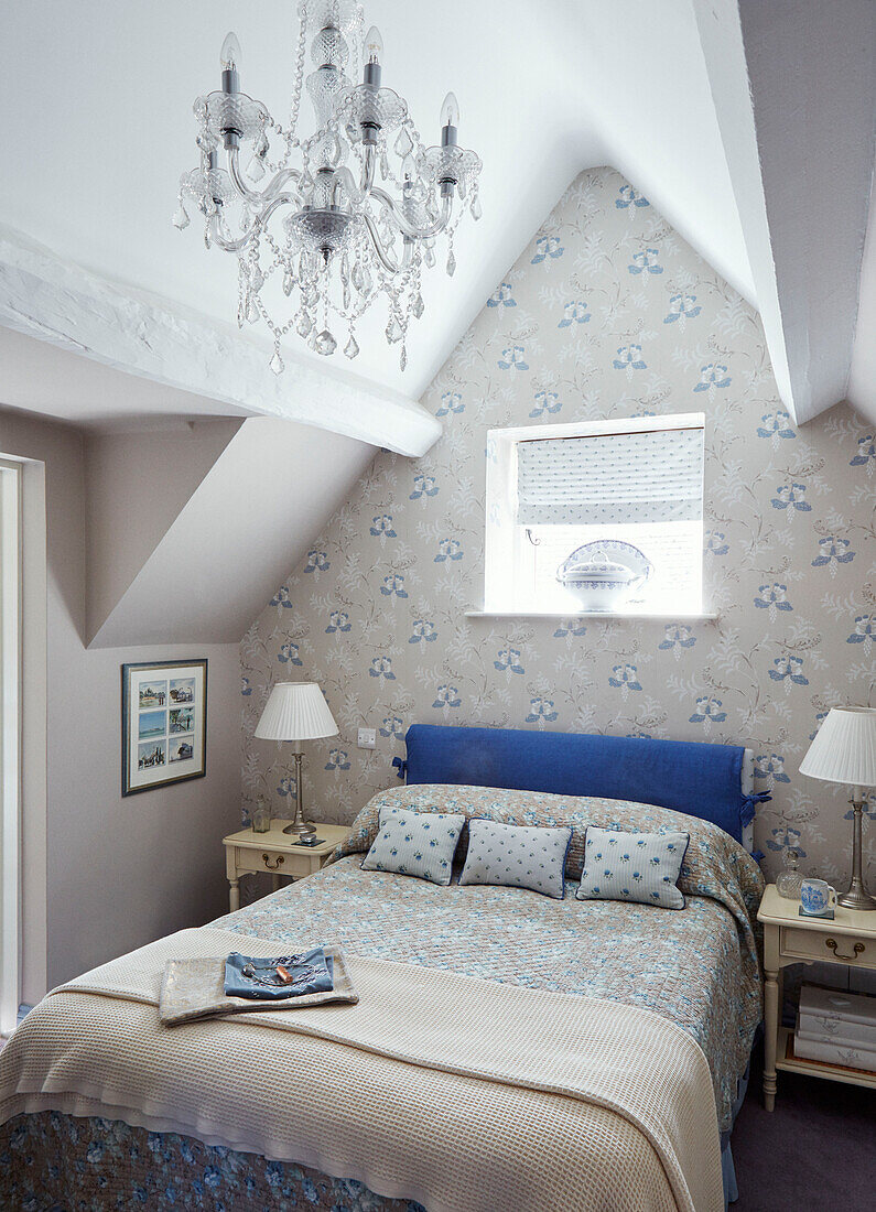 Gemusterte Tapete und Glaskronleuchter mit Doppelbett unter dem Fenster in einem Cottage in den Cotswolds, UK