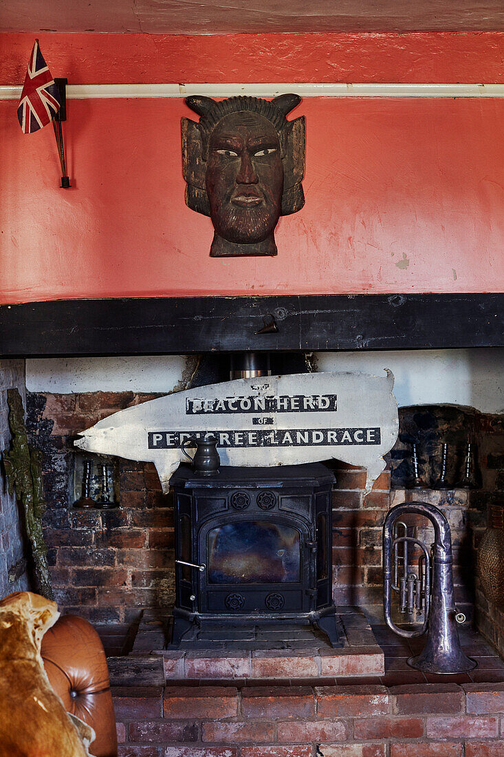 Mayan mask and vintage tuba with woodburning stove in brick fireplace Devon, UK