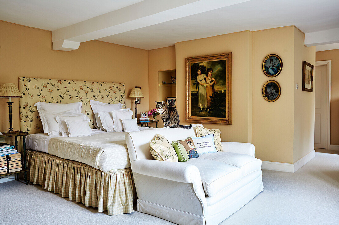 Zweisitzer-Sofa am Fußende des Bettes mit Volant und geblümtem Kopfteil in einem Haus in den Cotswolds, UK
