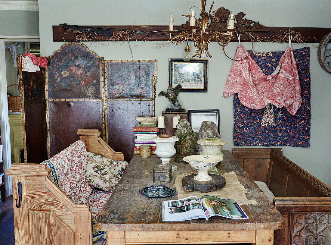 Zwei hölzerne Sitzbänke und ein Tisch mit Urnen und Büchern in einem Haus in Somerset, UK