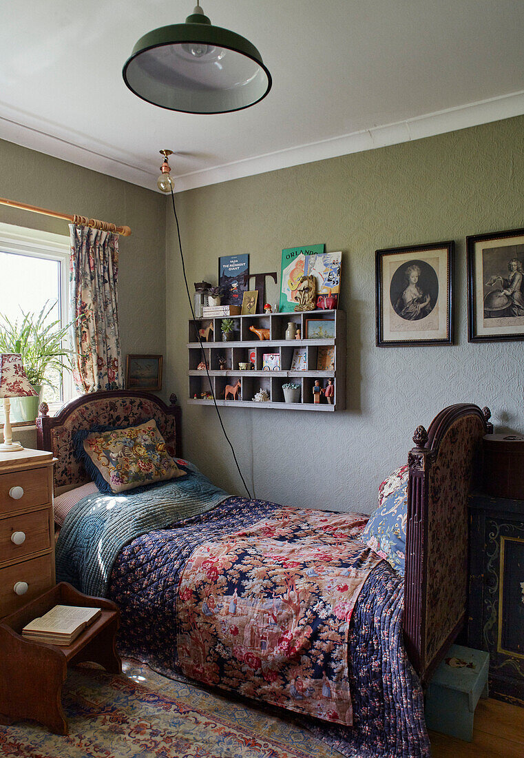 Wandregale und gerahmte Drucke über einem Einzelbett mit antiken Textilien in einem Haus in Somerset, UK