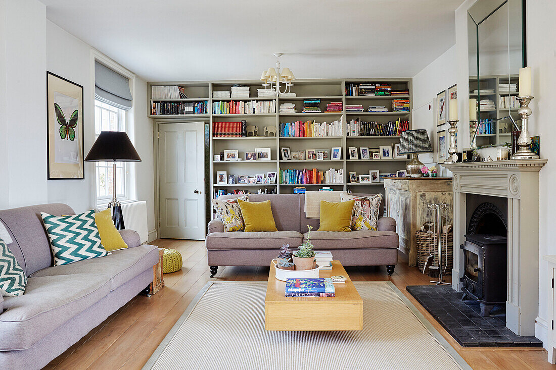 Family photos and books on shelving with sofas and woodburner in Oxfordshire living room, UK