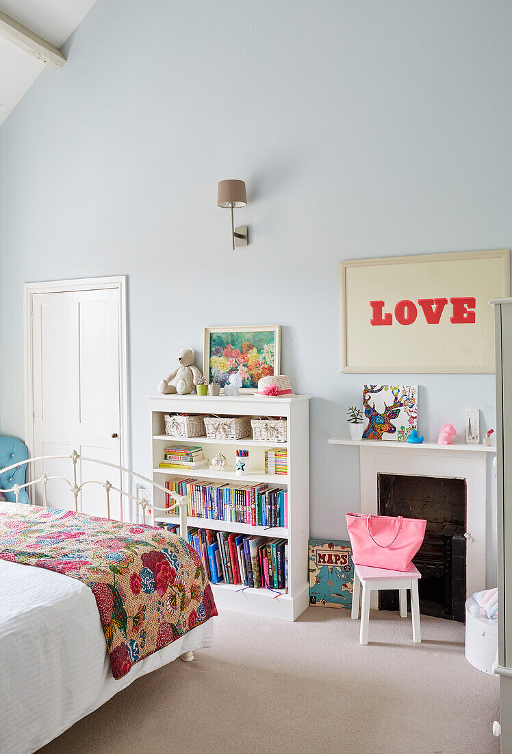 LOVE'-Druck und Bücherregal mit Patchwork-Quilt im Mädchenzimmer eines Hauses in Oxfordshire, UK