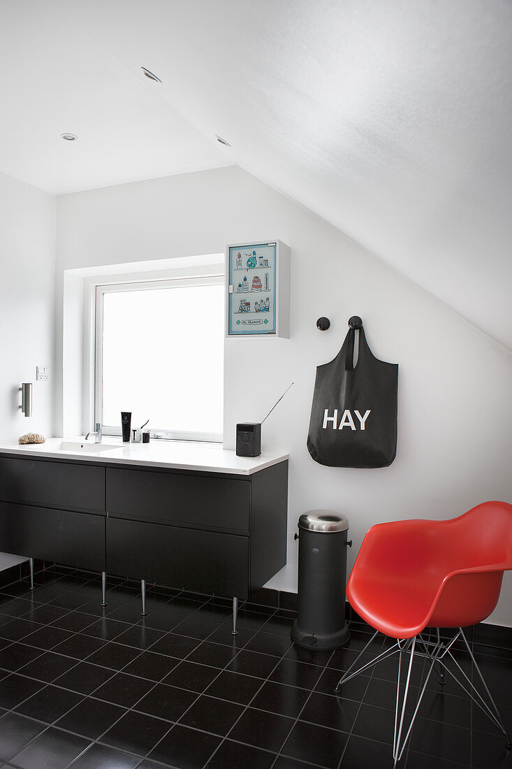 Red designer chair in black-and-white bathroom with sloping ceiling