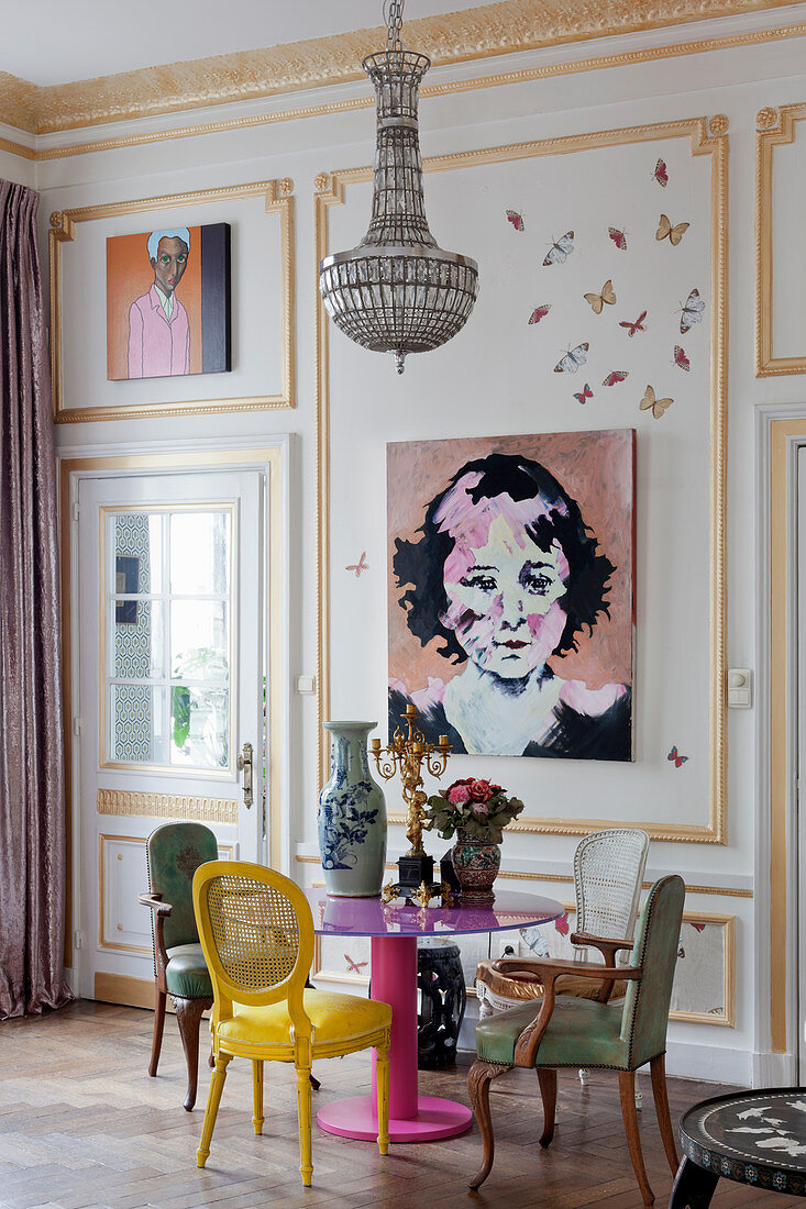 Various chairs around pink table next to paintings on panelled wall