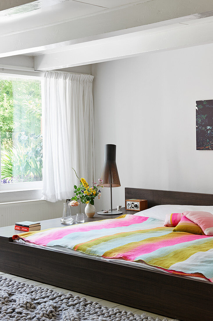 Doppelbett mit gestreifter Decke vor Fenster in hellem Schlafzimmer