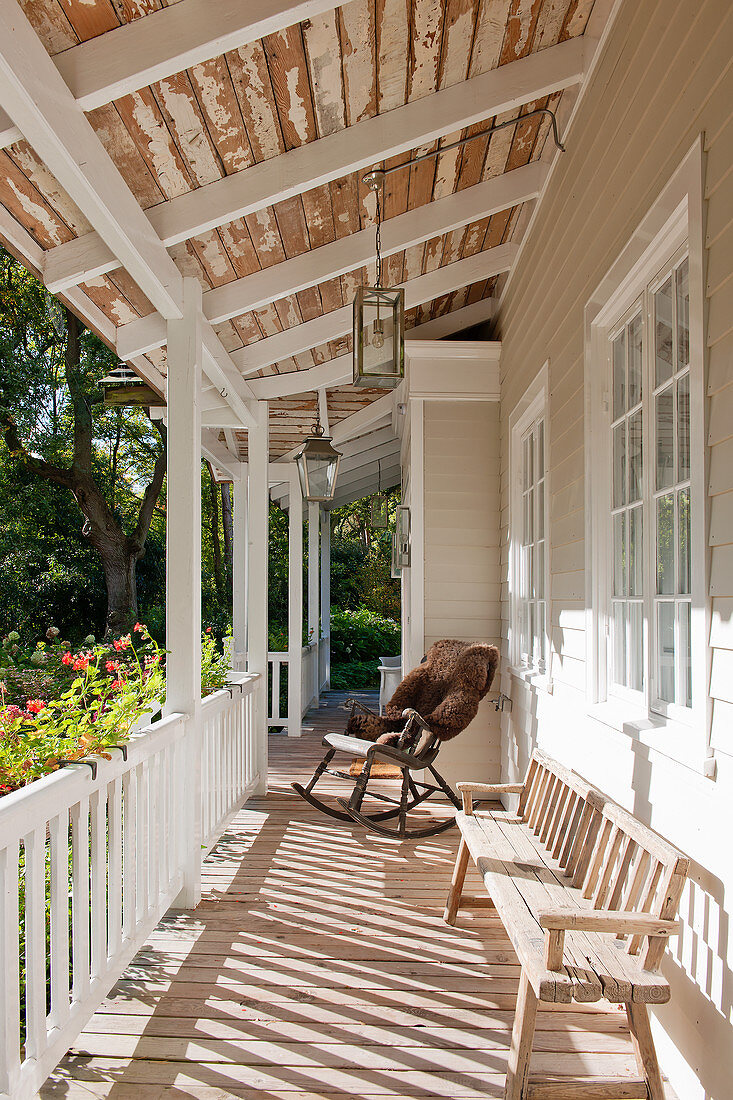 Rocking chair and old bench on veranda of white wooden house