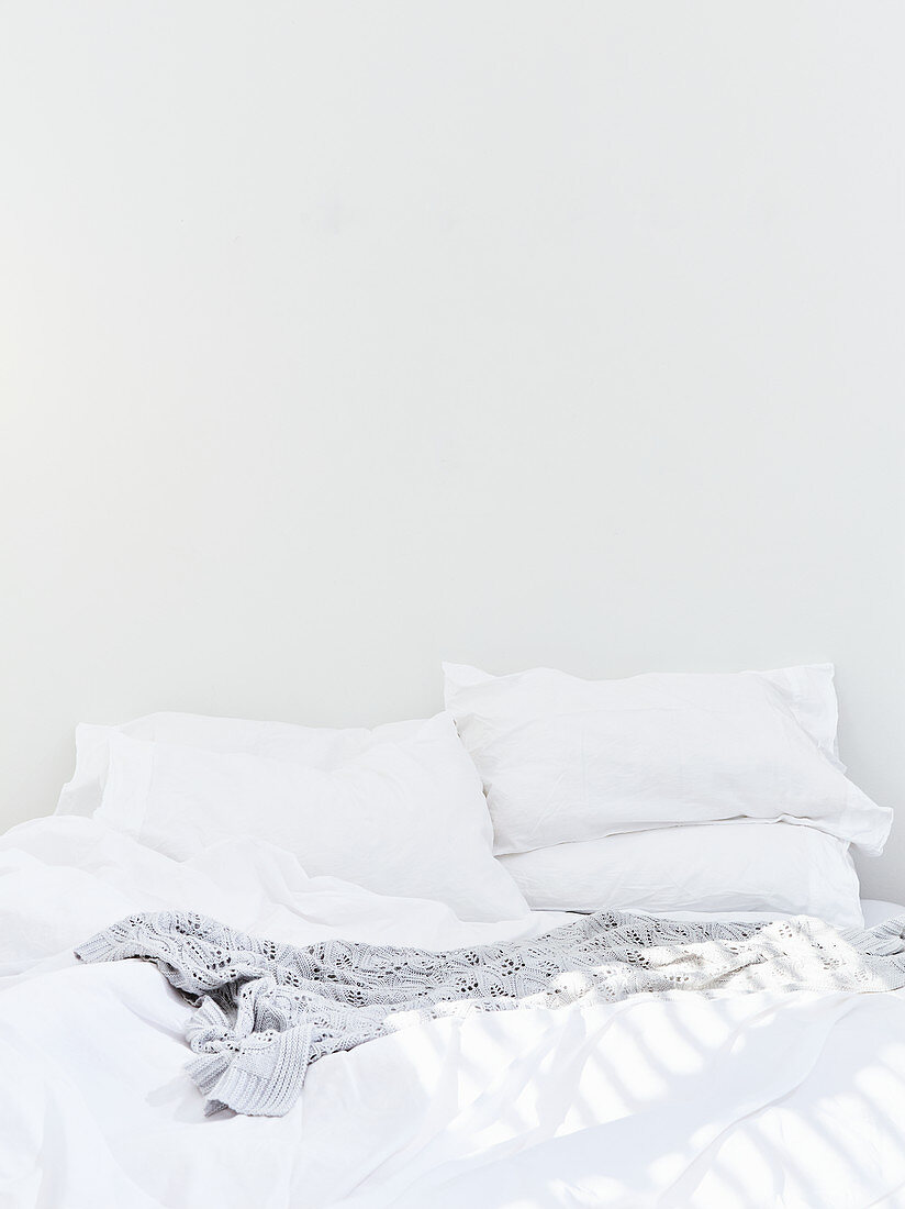 Doppelbett mit weißer Bettwäsche vor weißer Wand