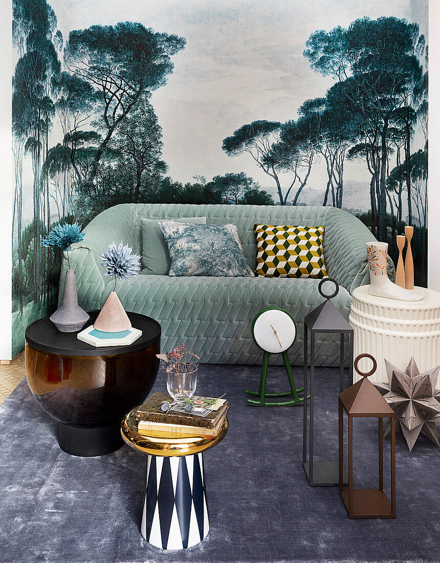 Coffee table, lanterns and green sofa against mural wallpaper with landscape motif