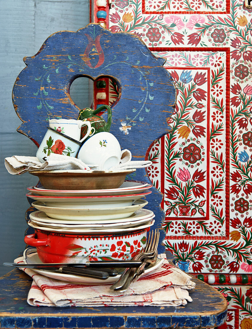 Crockery stacked on farmhouse chair in front of ethnic wall panel