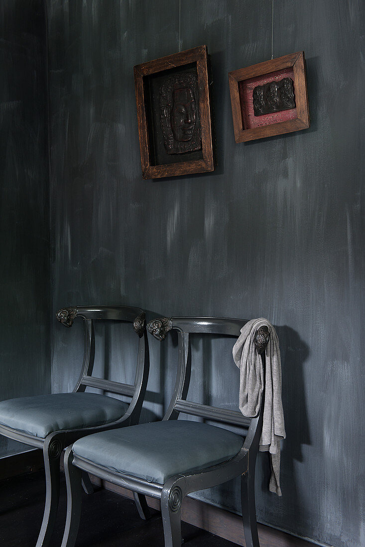 Zwei Stühle unter gerahmten Bildern vor schwarzer Wand