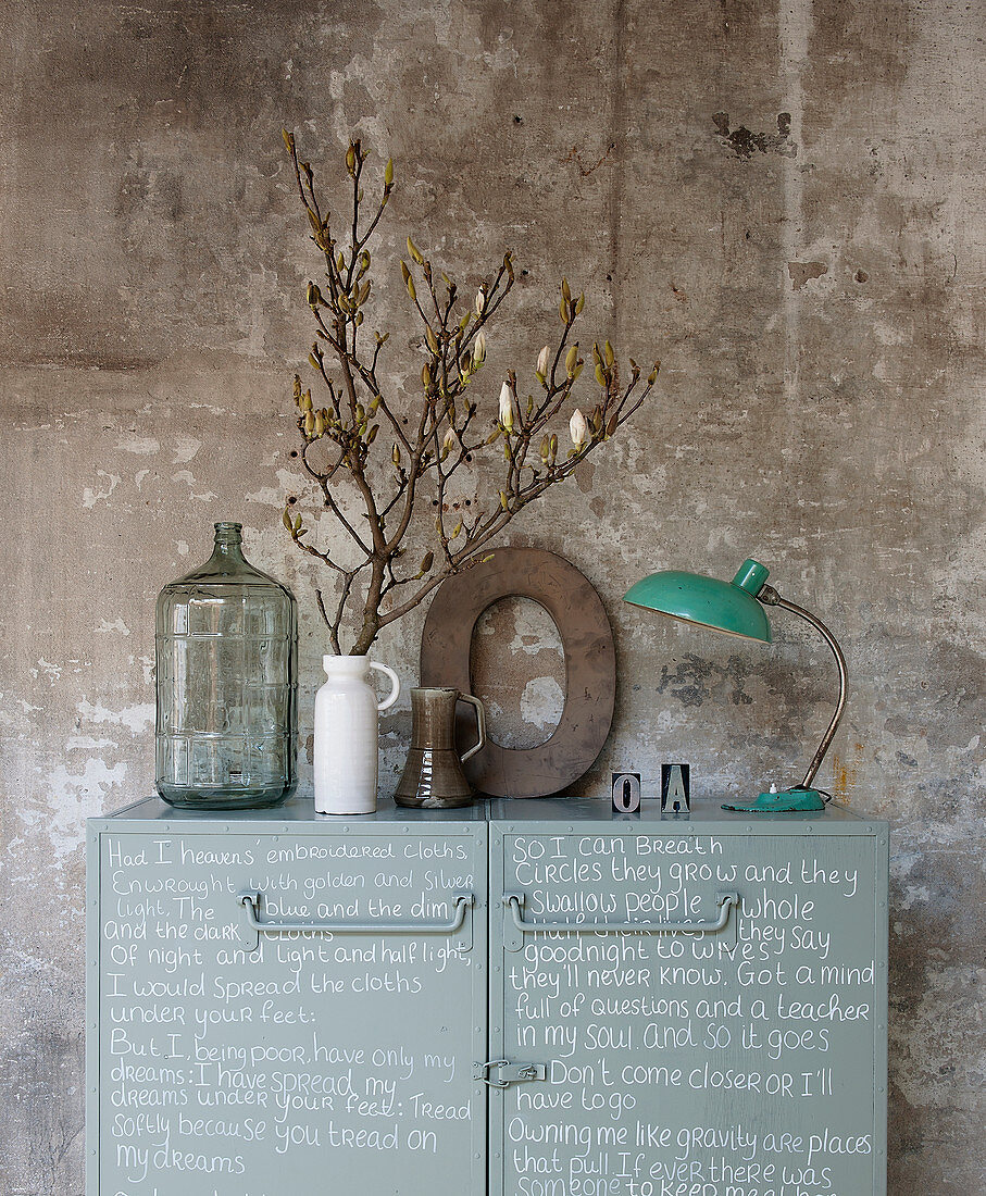 Metal cabinet decorated with handwriting, vase of twigs, decorative letter and table lamp