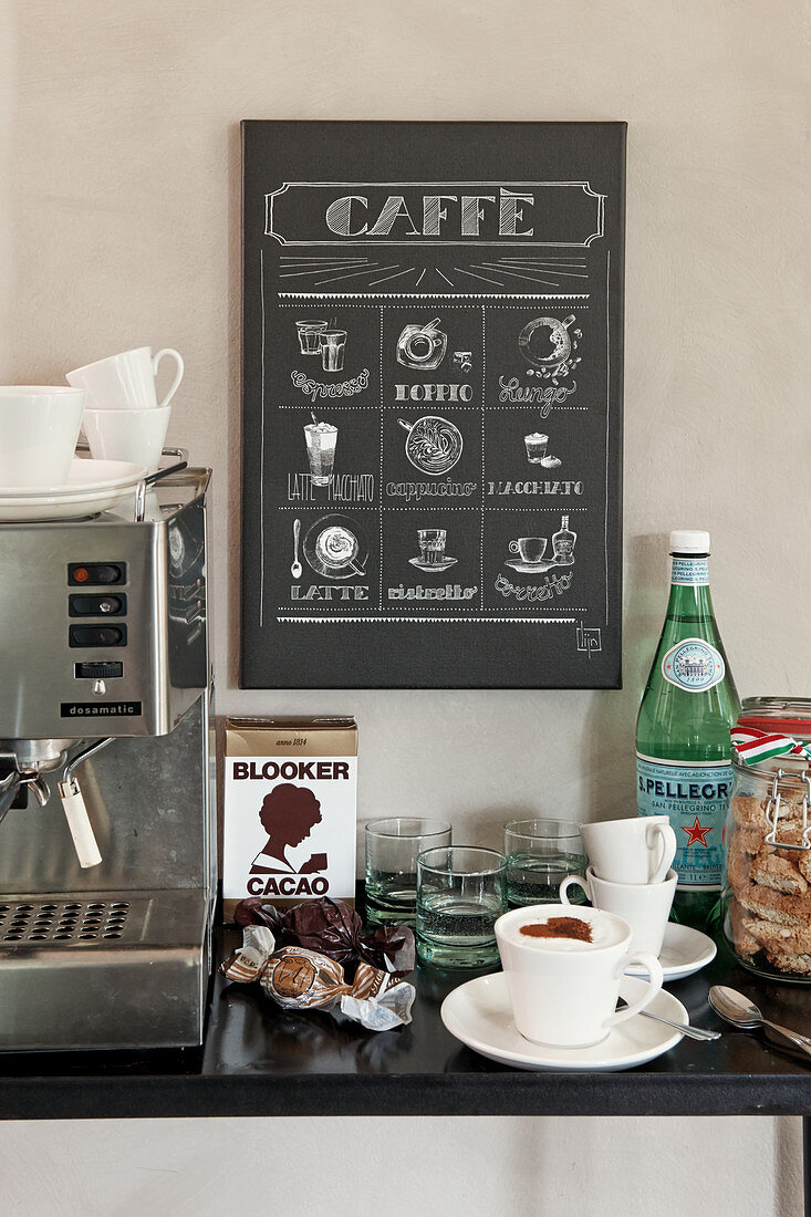 Kaffeeautomat, Cappuccionotasse, Mineralwasser vor Poster mit Kaffeemotiv