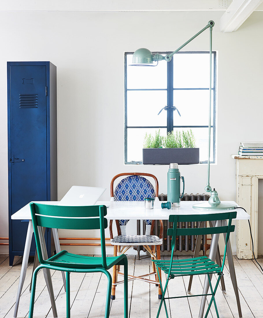 Esstisch mit verschiedenen Gartenstühlen, im Hintergrund blauer Metallschrank