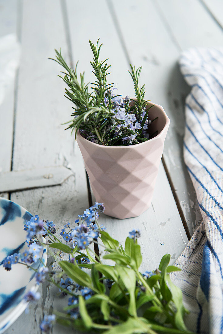 Flowering rosemary sprigs in a cup, forget-me-nots lying