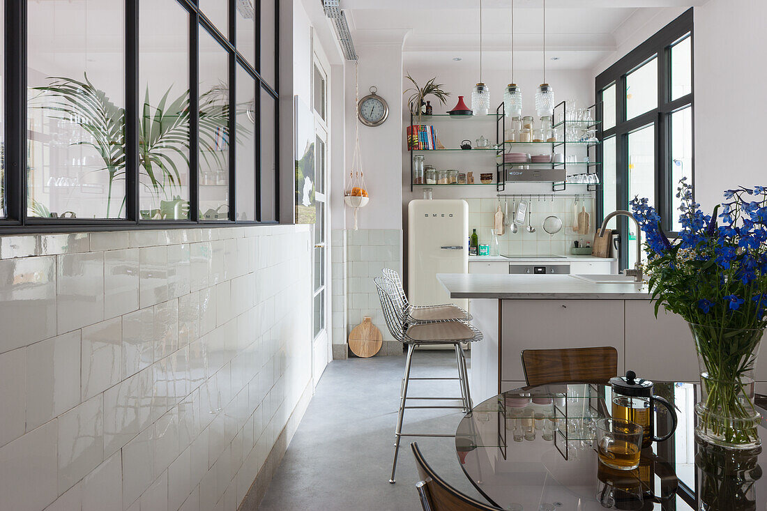 Bright kitchen with white tiles, metal bar stools and glass partition wall