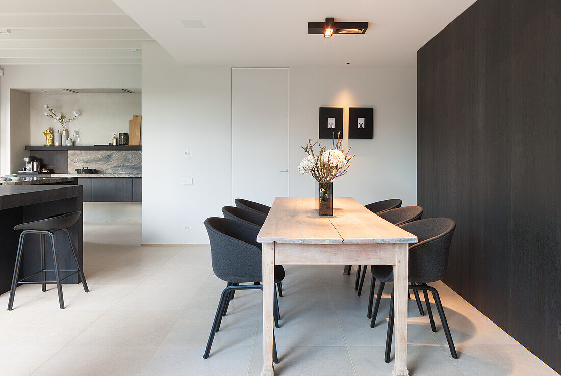 Wooden table and black chairs in modern dining area with kitchen in the background