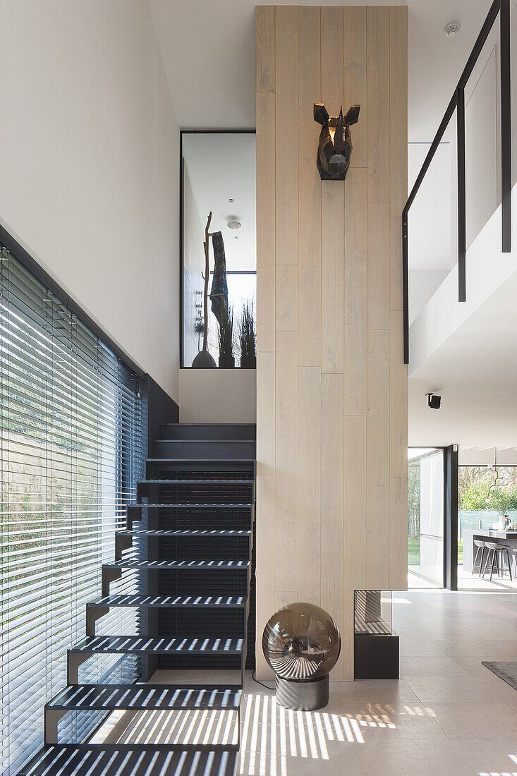 Staircase with black steps and light-colored wood paneling in a modern house