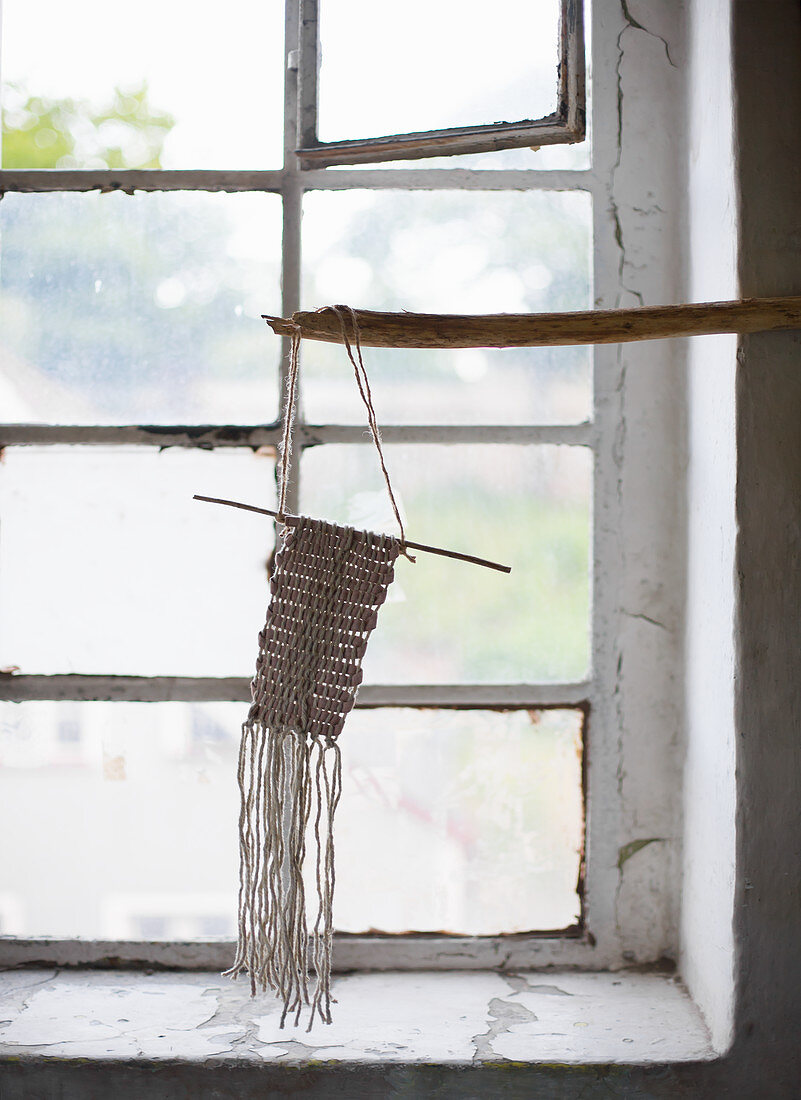 Macramé ornament hung from branch in front of window