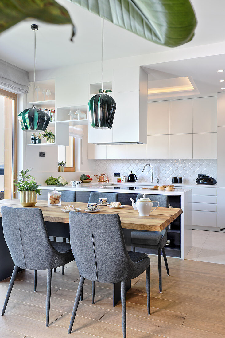 Grey upholstered chairs at wooden table next to modern, white open-plan kitchen