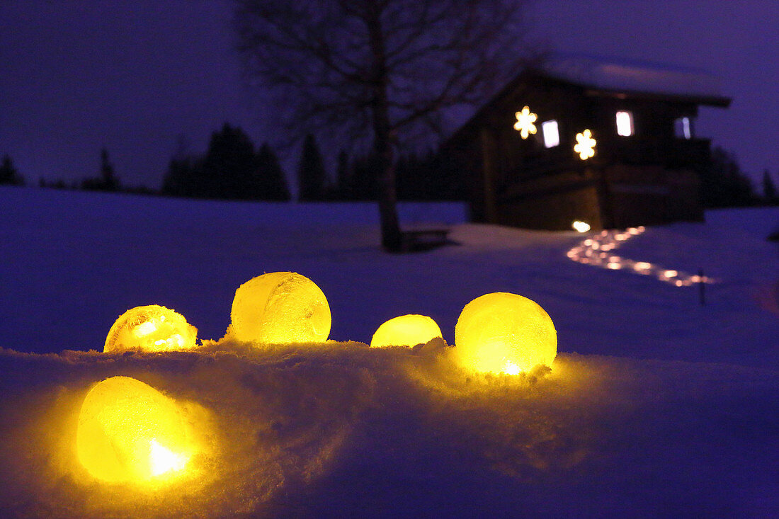 Windlichter aus Eis im Schnee vor beleuchtetem Weg zur Hütte