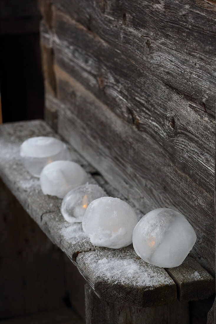 LED candles in ice candle lanterns on rustic wooden bench outside cabin