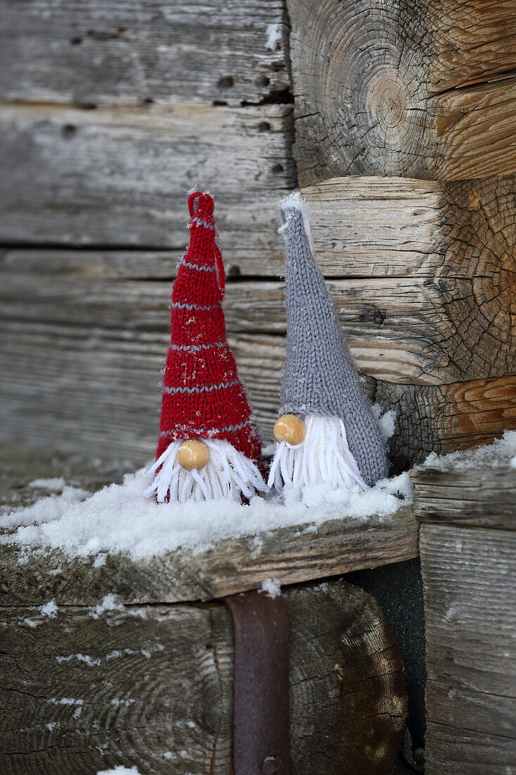 Knitted winter decorations in shapes of gnomes on rustic wood with snow