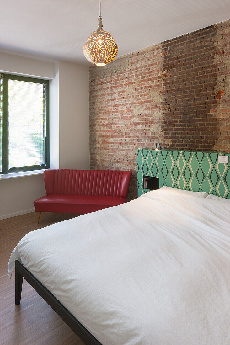 Red leather couch and bed in front of brick wall in bedroom