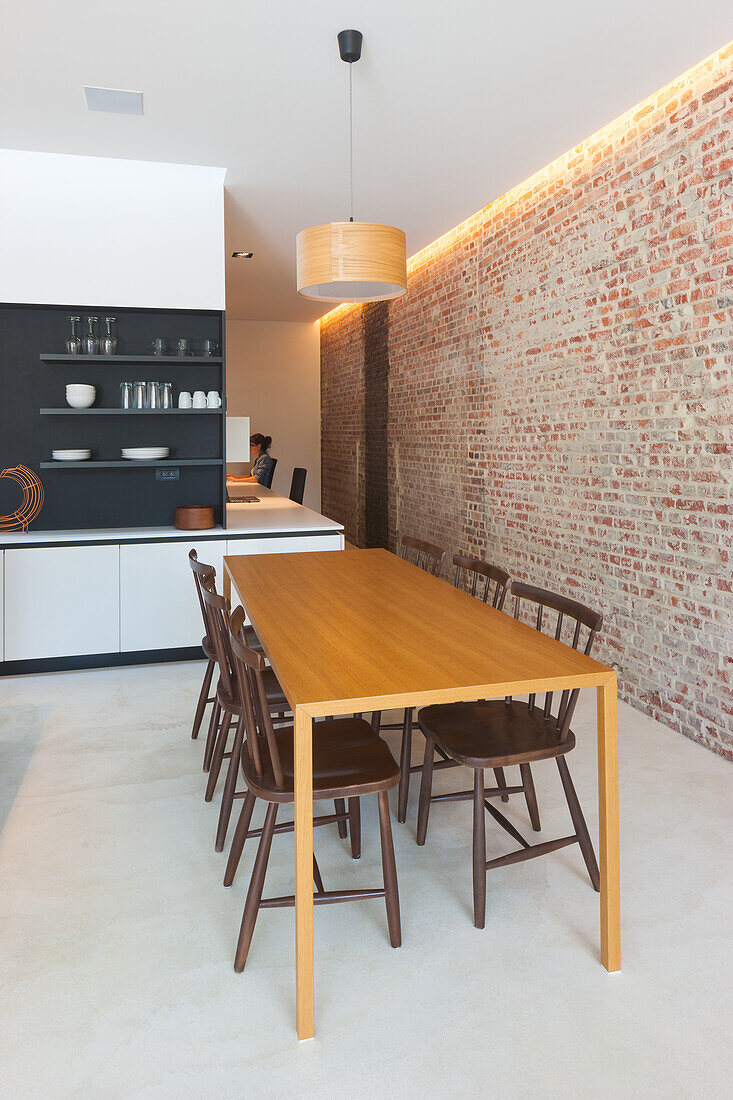 Esstisch aus Holz und dunkle Stühle, Backsteinwand in moderner Wohnküche