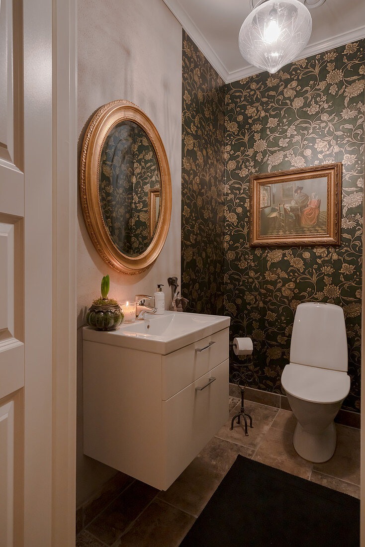 Elegantes Toilettenbad mit floraler Tapete und Goldrahmenspiegel