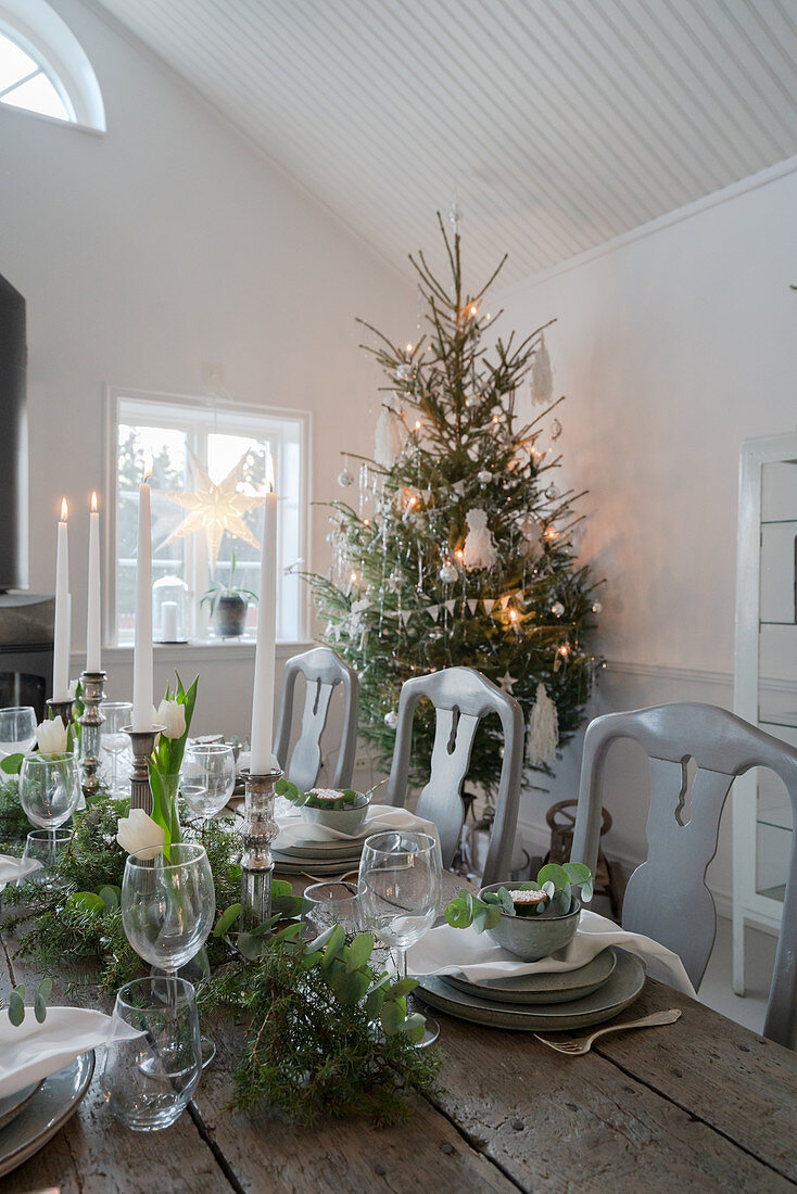 Festively set wooden table decorated in white, green and grey for Christmas meal