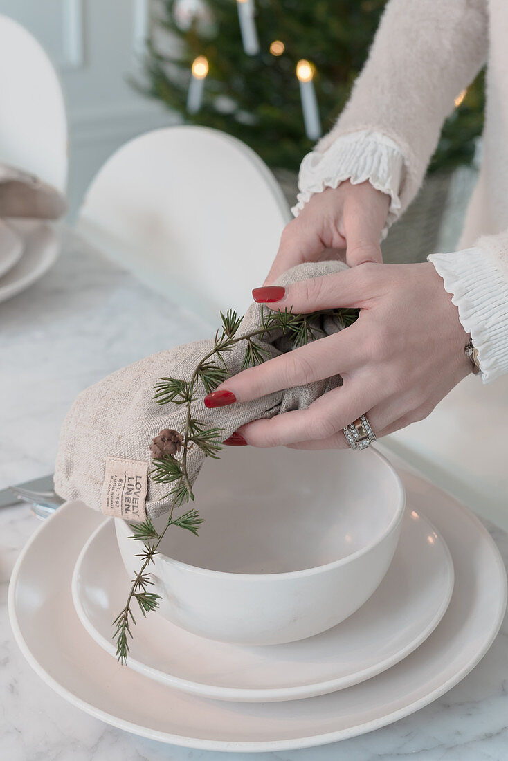 Hands placing napkin and larch branch on set table