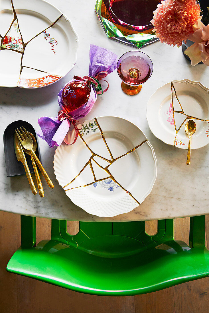 Gedeckter Tisch mit Tellern aus Scherben und goldenem Besteck