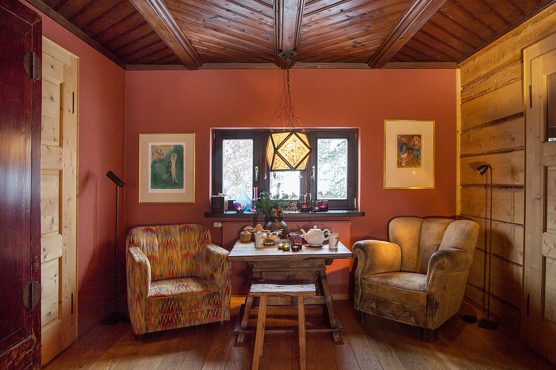 Rustikales Esszimmer mit Sesseln am gedeckten Tisch vor roter Wand