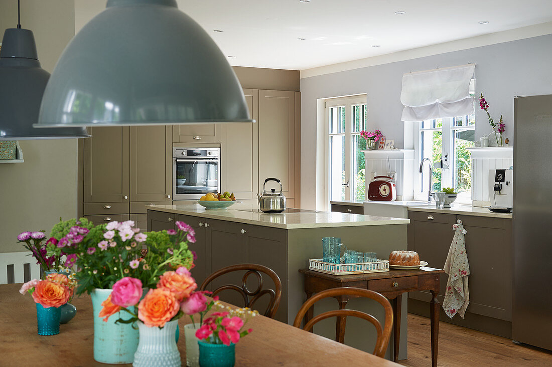 Blick über Holztisch mit Blumendeko in die Küche mit Mittelblock