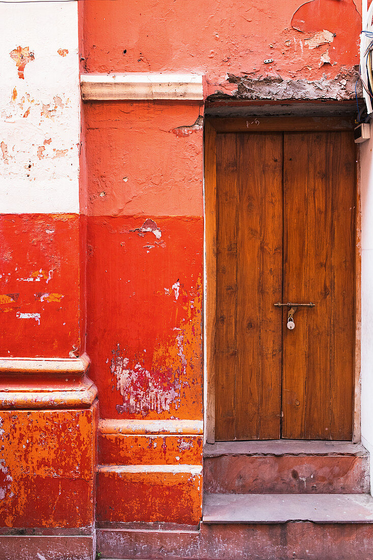 Wooden door in red wall with peeling paint
