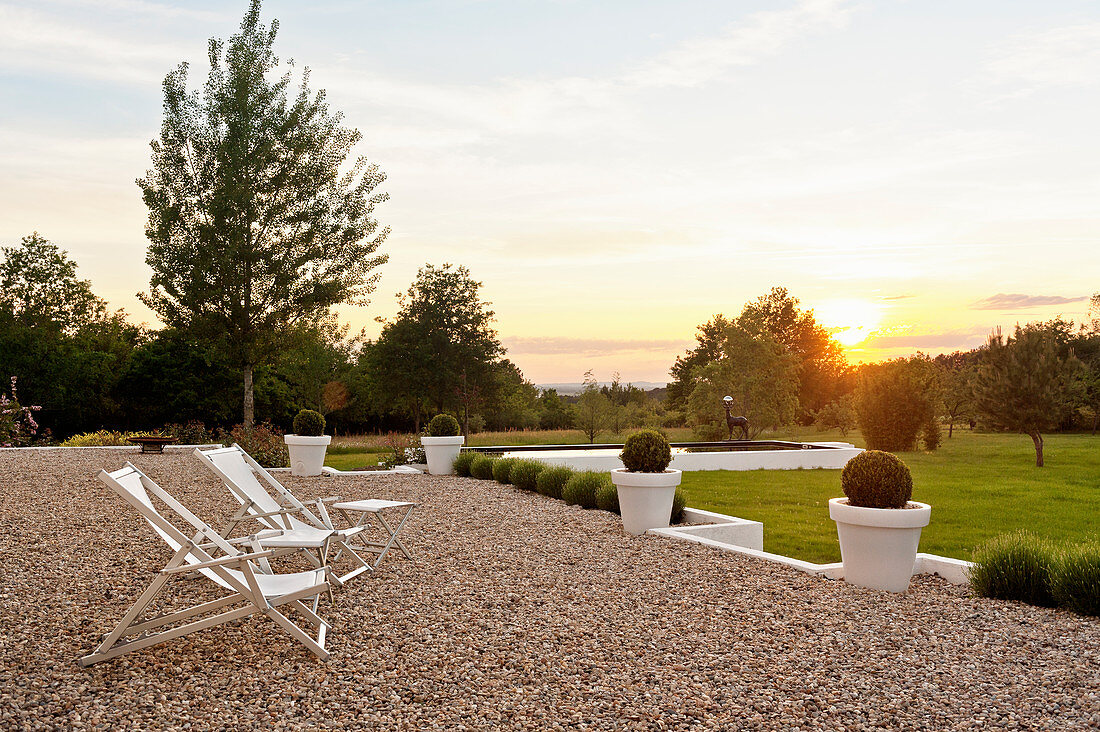 Pair of deck chairs on gravel terrace with garden views at sunset