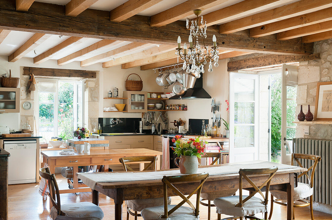 Rustic kitchen with French wooden dining table, ceilings beams, glass chandelier and traditional Camargue-style dining chairs