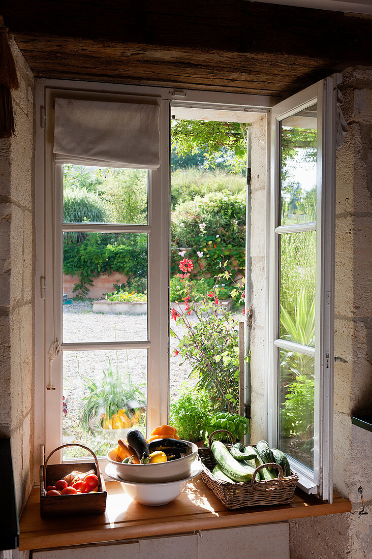 Fresh vegetables arranged in baskets on the sill of an open window set into a thick stone wall